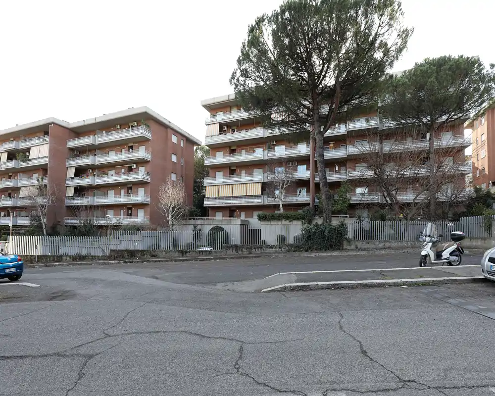 Vista esterna a livello strada di un edificio residenziale multipiano con balconi, alberi e veicoli parcheggiati; utile per mostrare la facciata e il contesto del quartiere.