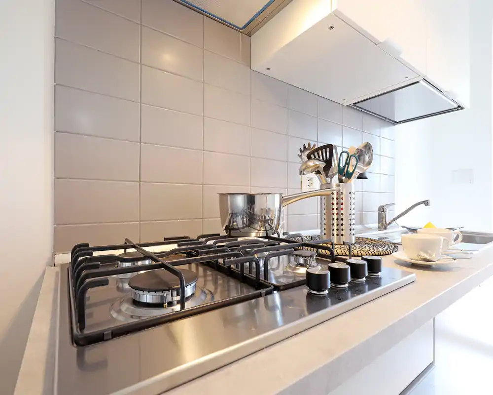 Piano cucina moderno e luminoso con piano cottura a gas, pentola in acciaio e utensili ordinati: spazio pulito e funzionale ideale per cucinare.
