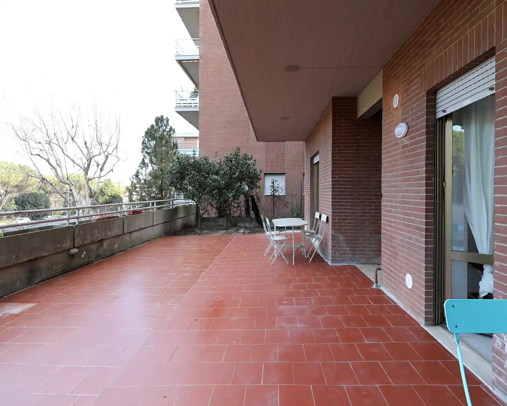 Ampia terrazza coperta con pavimento in cotto rosso, piccolo tavolo e sedie, e ringhiera con vista sugli alberi — ideale per relax o pranzi all'aperto.