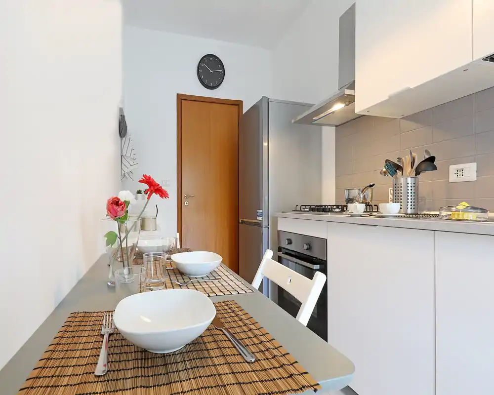 Cucina moderna e luminosa con penisola apparecchiata per due; mobili chiari, frigorifero in acciaio e forno incassato rendono lo spazio funzionale e ordinato.