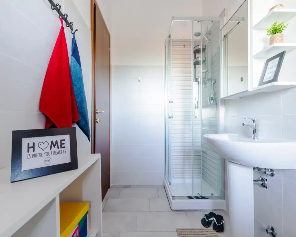 Bagno moderno e luminoso con cabina doccia in vetro, lavabo a colonna e scaffalatura ordinata; stile pulito e minimal con buona luce naturale.
