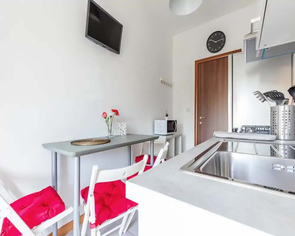 Angolo cottura compatto e luminoso con tavolo da pranzo, sedie pieghevoli imbottite e piano cottura moderno — perfetto per un monolocale in città.