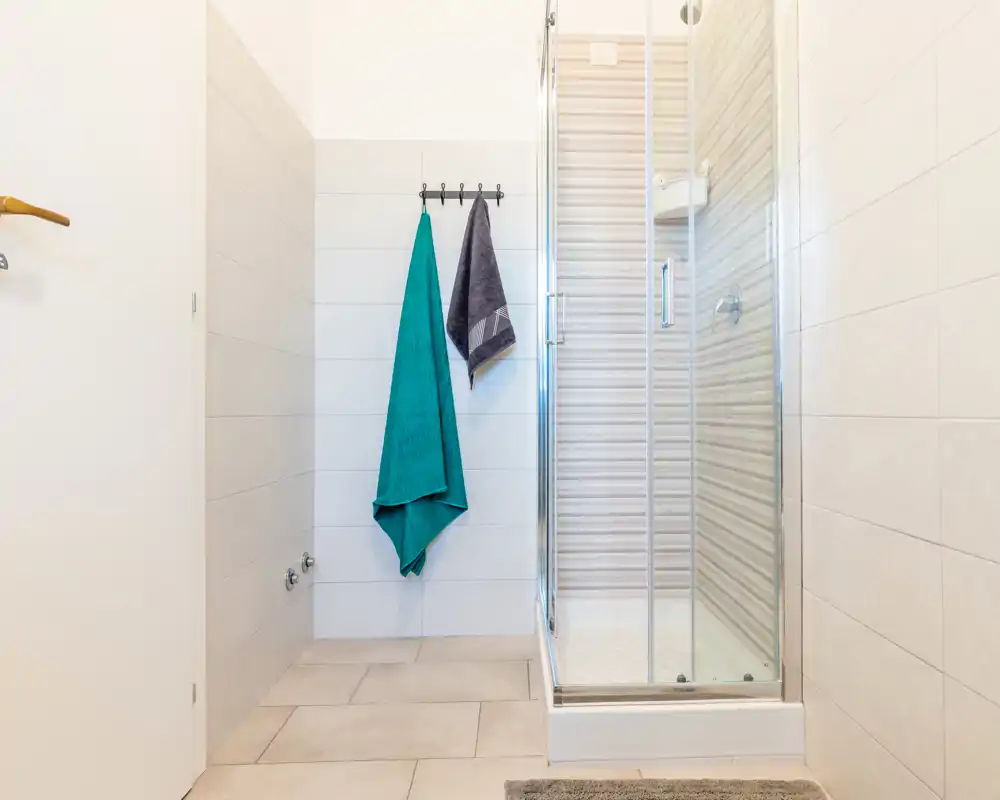 Bright, modern bathroom with a glass-enclosed shower, tiled walls and two hanging towels. Clean, minimal design ideal for rental listings.