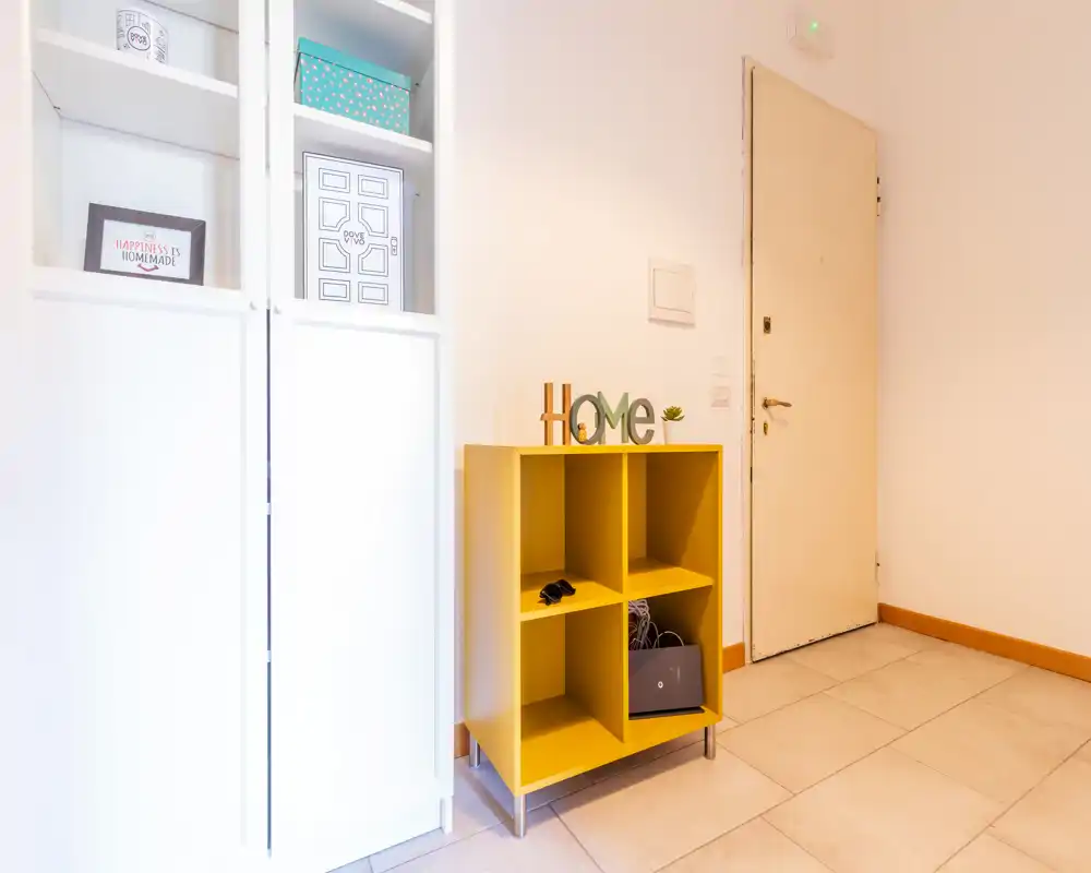 Bright, tidy entrance area with a yellow cubby storage unit, decorative 'Home' sign and a white closet beside the front door — ideal for welcoming guests and organizing shoes or small items.