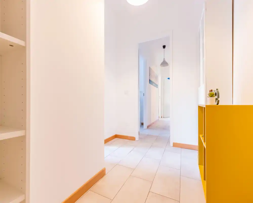 Bright, minimal entrance hallway with tiled floor, white walls and a small yellow storage unit providing a cheerful accent.