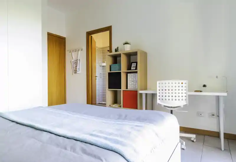 Bright, modern bedroom with a neatly made double bed, a white desk and chair, and a wooden cube shelf for storage — clean minimal styling and natural light ideal for rental listings.
