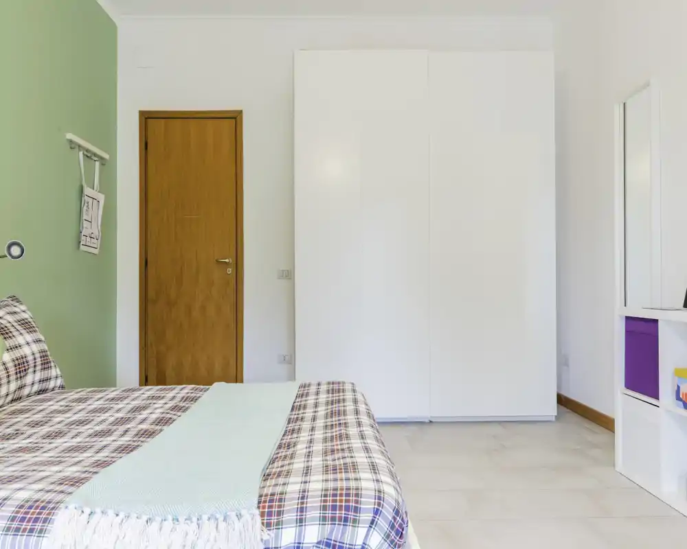 Bright, modern bedroom with a large bed in patterned textiles, a white wardrobe and simple, clean decor ideal for rental listings.