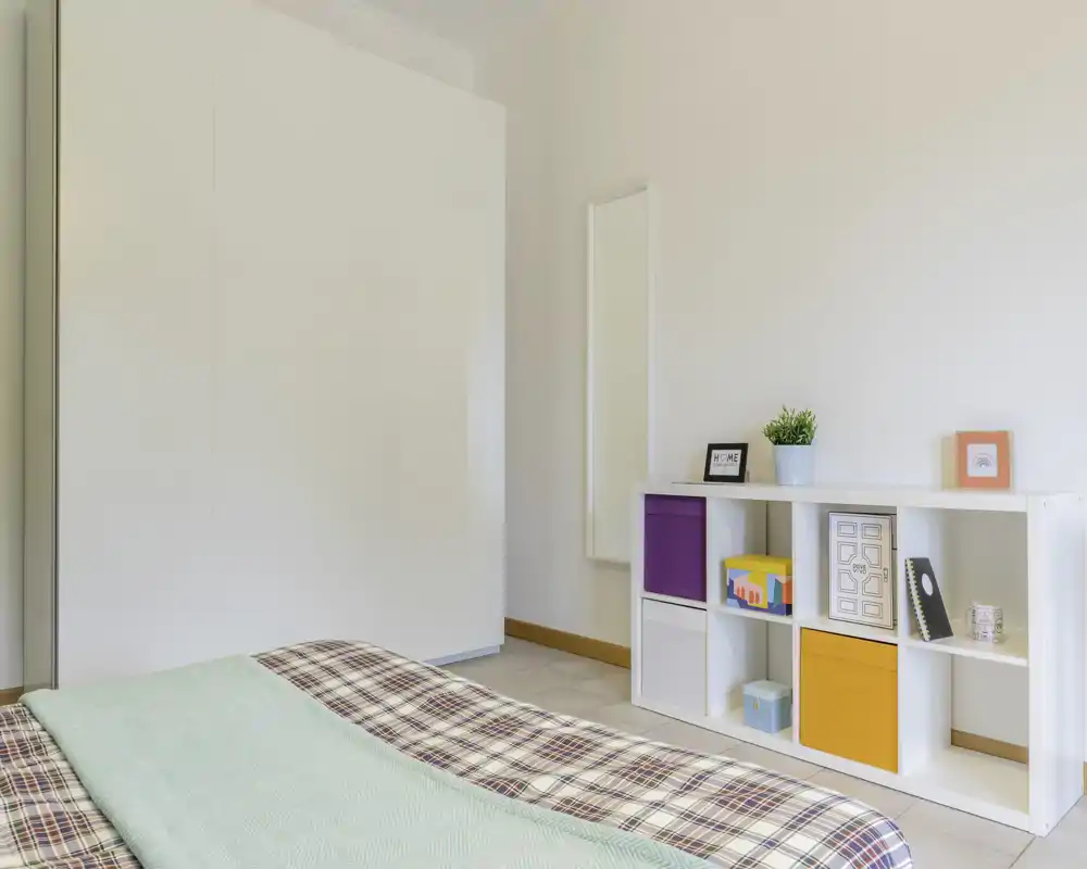 Bright, minimalist bedroom with a patterned duvet and a low shelving unit with colorful storage cubes — ideal for a clean, modern rental listing.