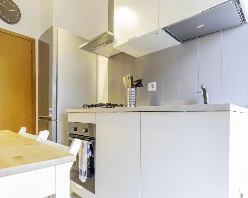 Modern compact kitchen with built-in oven, gas hob, stainless fridge and a wooden dining surface — bright, clean and practical for short stays.