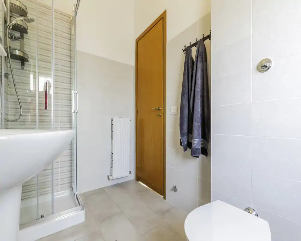 Clean, modern bathroom with a glass shower enclosure, pedestal sink and wall-mounted toilet. Neutral tiles and natural light create a fresh, welcoming space.