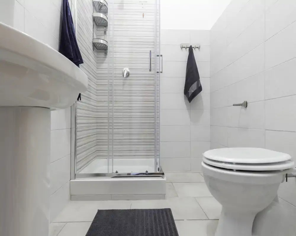 Bagno moderno e pulito con box doccia in vetro, lavabo a colonna e wc. Piastrelle chiare e asciugamani scuri danno un aspetto minimalista.