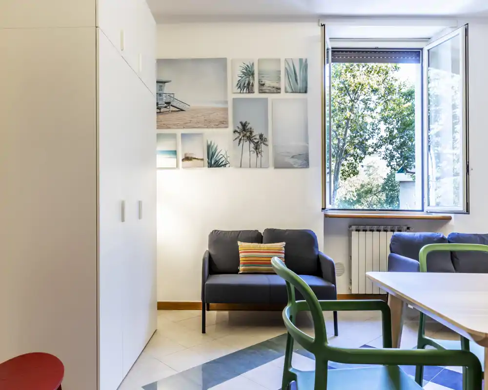 Bright, modern living area with a small sofa, decorative cushion and gallery wall next to a large open window offering abundant natural light.
