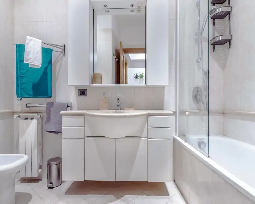 Bright, modern bathroom with a built-in sink cabinet, large mirror, bathtub with glass screen and tidy accessories—clean and well-lit space ideal for listings.