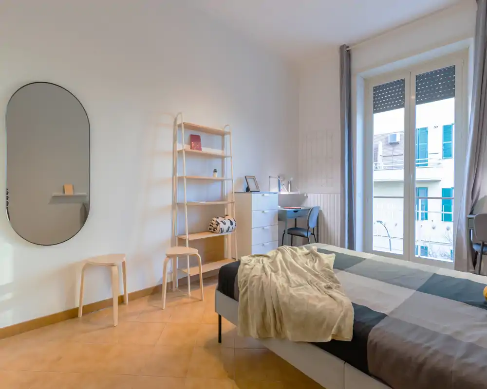 Bright, modern bedroom with a large window, tidy shelving and a comfortable double bed dressed in neutral linens — ideal for a welcoming rental listing.