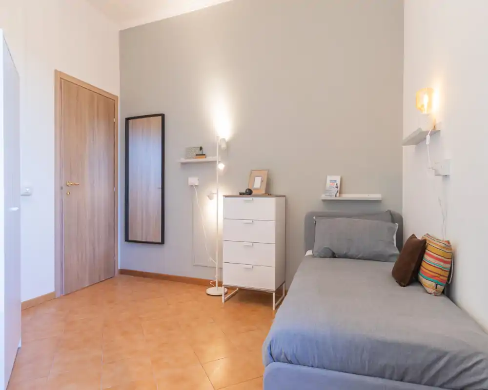 Chambre simple et accueillante avec lit bien fait, éclairage d’appoint chaleureux et mobilier moderne. Palette neutre et agencement soigné pour une ambiance reposante, parfaite pour un court séjour.