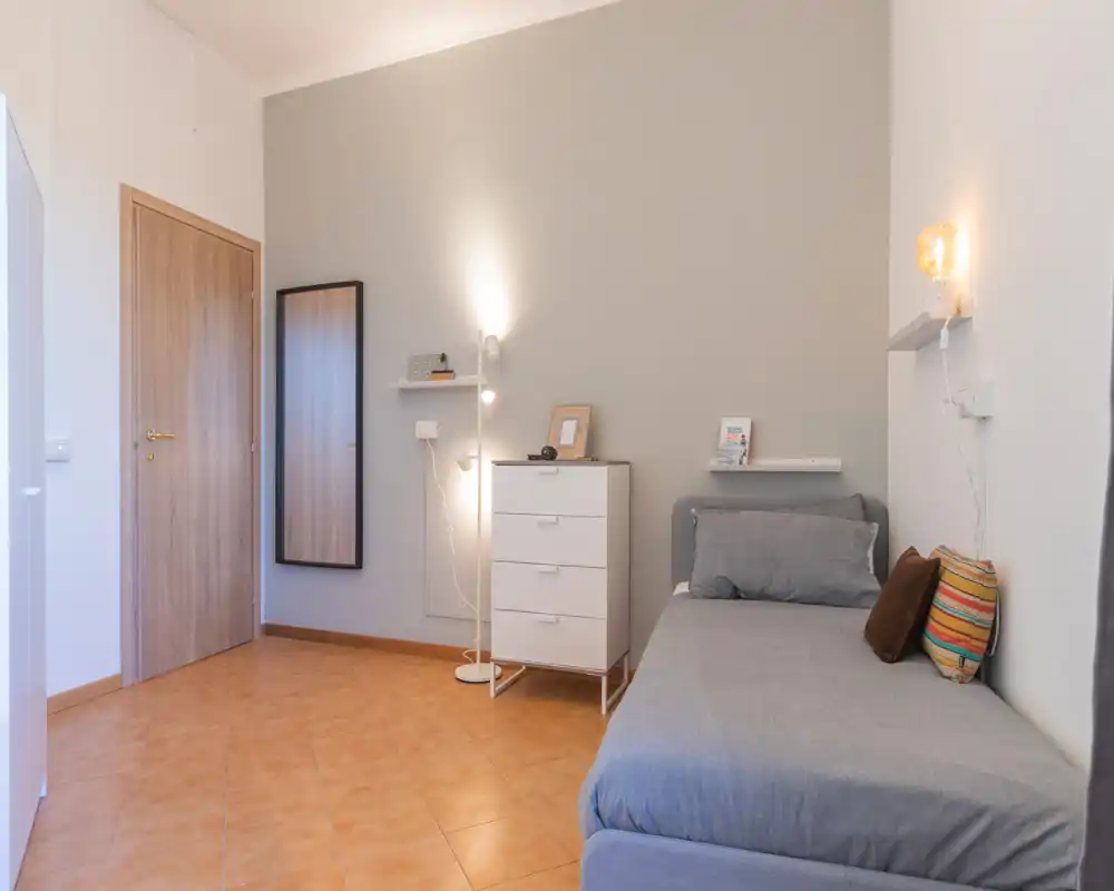 Chambre simple lumineuse et soignée avec lit bien fait, lampe de chevet et commode—parfaite pour un séjour confortable.