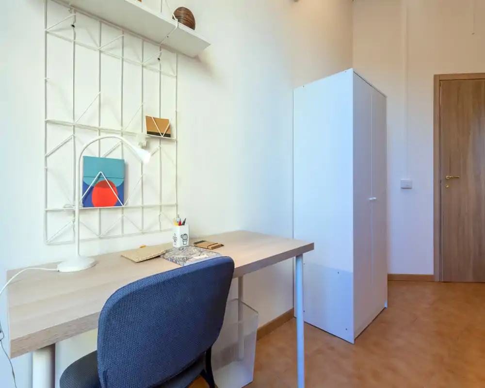 Coin chambre lumineux aménagé en espace de travail avec bureau en bois, lampe de bureau et armoire ; tons neutres et lignes épurées pour une ambiance calme.