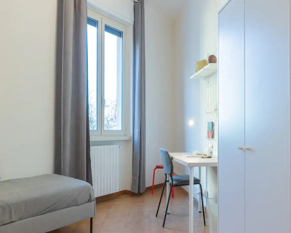 Chambre lumineuse et minimaliste avec lit simple, bureau et armoire ; grande fenêtre apportant une belle lumière naturelle et coin bureau soigné.