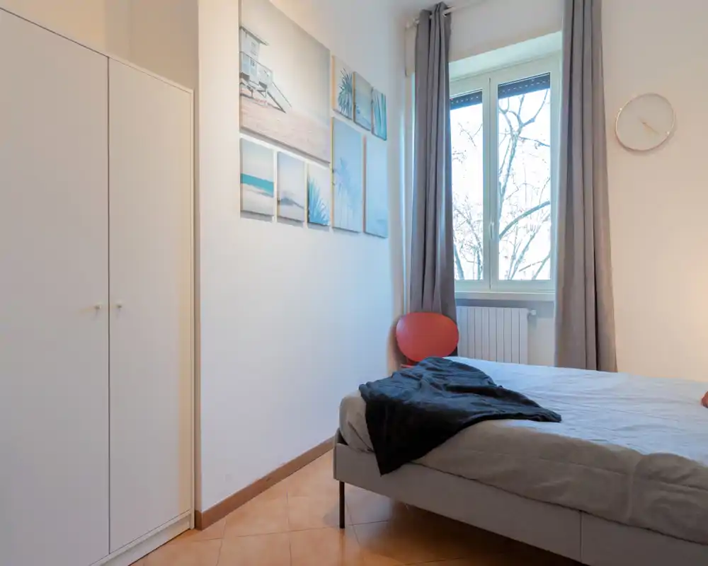 Camera da letto luminosa e semplice con letto matrimoniale, quadri decorativi e finestra che dona luce naturale — ideale per un soggiorno accogliente.