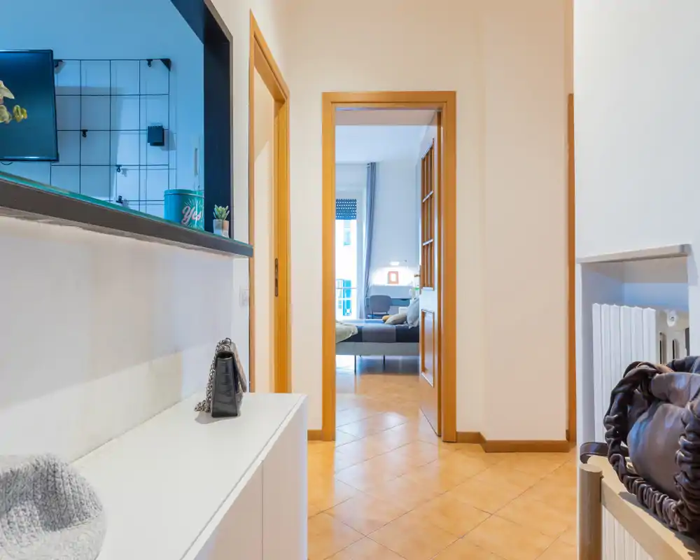 Bright, tidy entrance hallway with a view through to a bedroom. Neutral tiles and light-painted walls create a welcoming first impression.