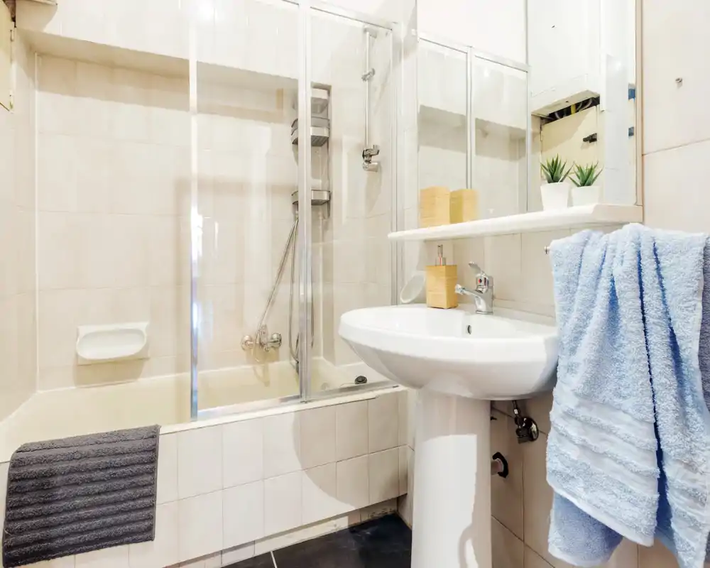 Clean, well-lit bathroom with a combined bathtub and shower, pedestal sink, mirrored cabinet and fresh towels—ideal for rental photos highlighting bathroom amenities.