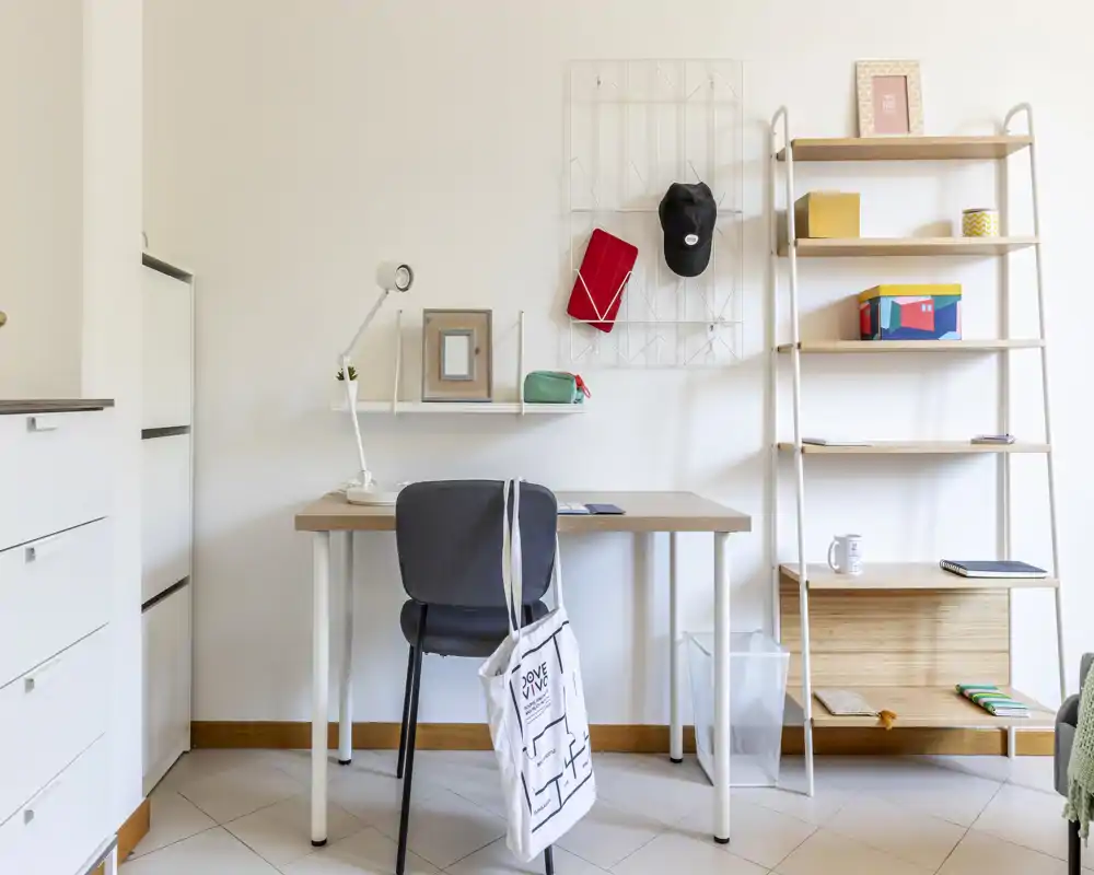 Espacio de trabajo luminoso y ordenado con escritorio de madera, silla y estantería. Estilo minimalista con lámpara de escritorio y pequeños objetos decorativos; perfecto para teletrabajo o estudio.