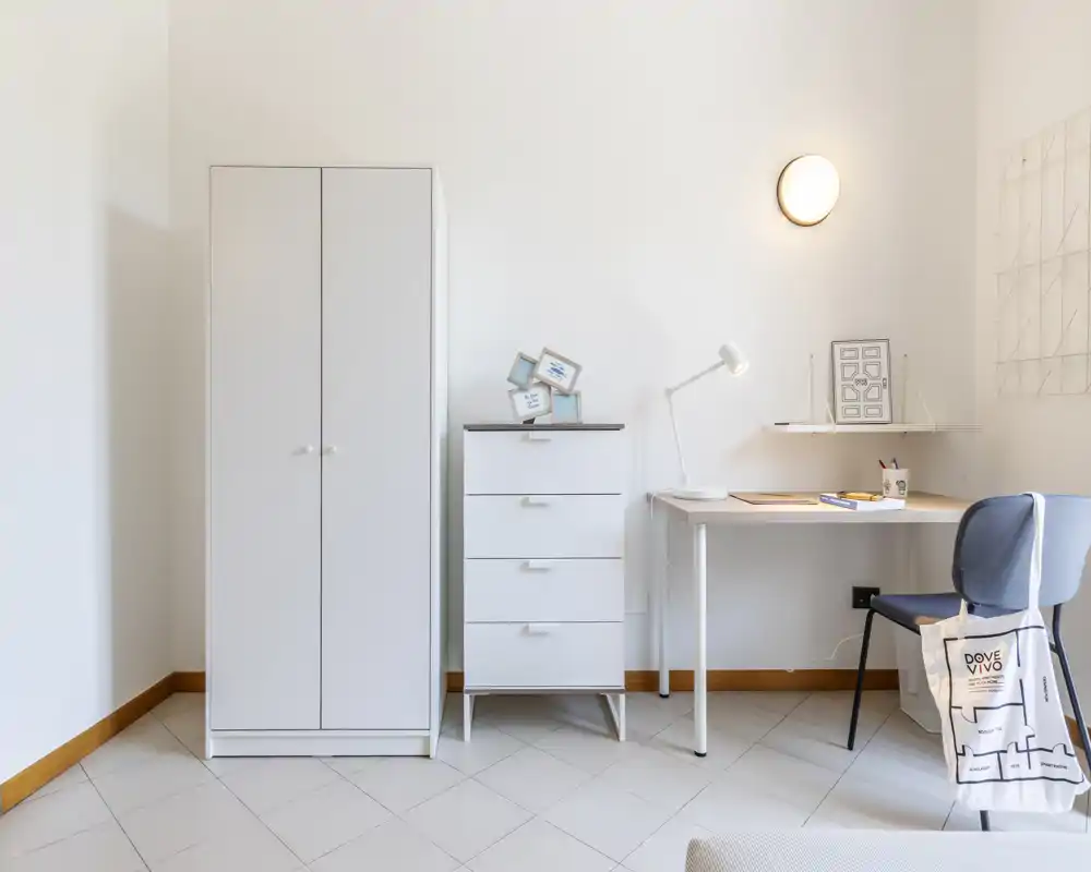 Minimal, bright bedroom corner with white wardrobe, chest of drawers and a small desk — tidy and well lit, suitable for a compact rental.