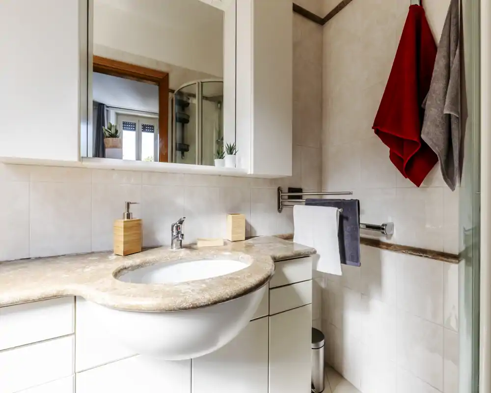 Baño moderno y luminoso con encimera de mármol y lavabo, espejo, toalleros y paredes alicatadas — bien iluminado y ordenado.