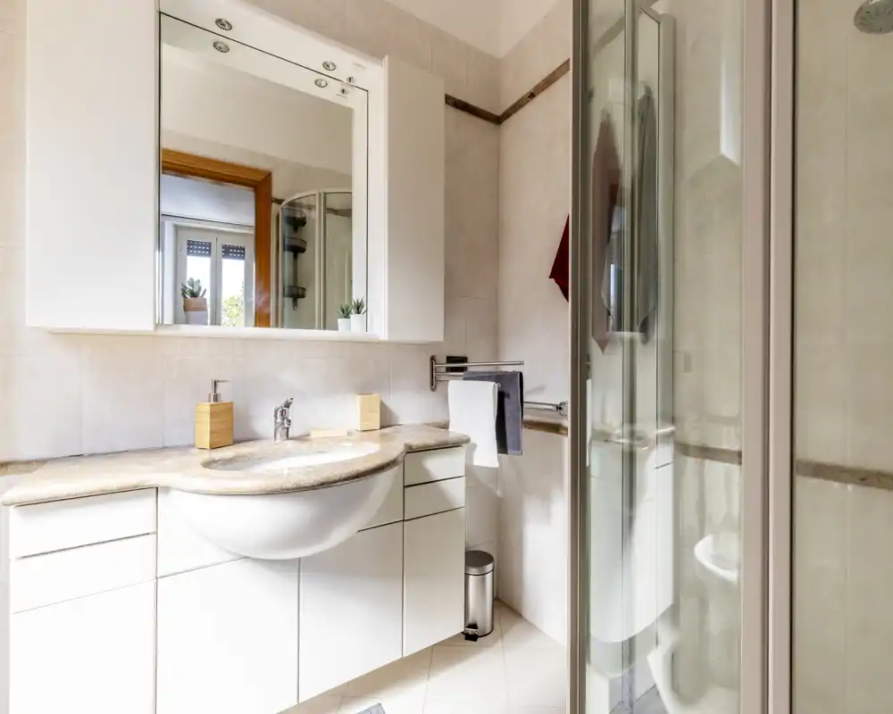 Baño moderno y luminoso con encimera de lavabo efecto mármol, mueble con espejo, ducha con mampara de cristal y toalleros.