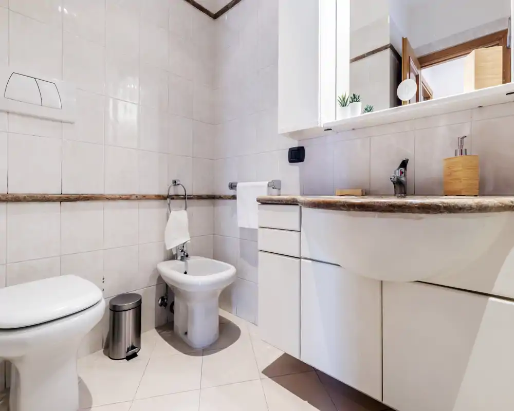 Baño moderno y limpio con paredes alicatadas, inodoro, bidé y lavabo con mueble y espejo; diseño luminoso y neutro ideal para anuncios.