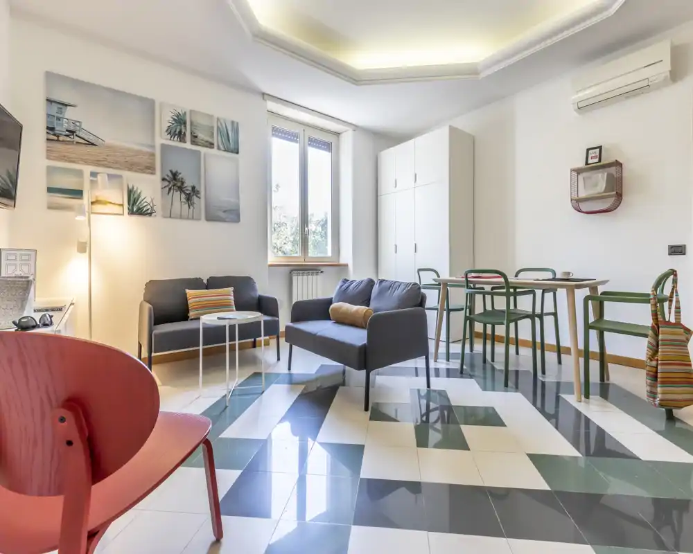 Sala de estar moderna y luminosa con suelo de baldosas geométricas, dos sofás, mesa de comedor y arte en la pared — perfecta para un alquiler urbano con estilo.