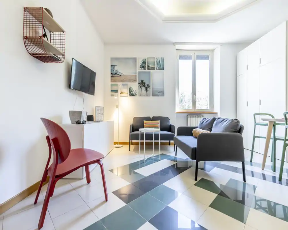Salón moderno y luminoso con sofá gris, sillón, cuadros decorativos y suelo de baldosas con patrón — una zona de estar elegante y acogedora con luz natural.