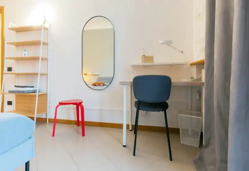 Angolo camera compatto e luminoso con un angolo del letto visibile, scrivania e specchio — luminoso e ben arredato, ideale per affitti brevi.