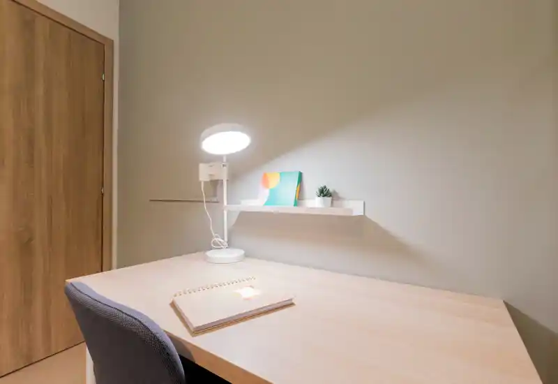 Bright, minimal workspace with a wooden desk, desk lamp, chair and a small shelf with decor — ideal for focused work or study.