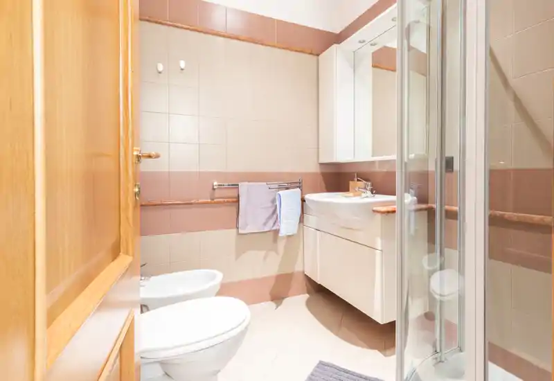 Bright, modern bathroom with a shower cabin, wall-mounted sink with storage, bidet and toilet; neutral beige tiles and a mirrored cabinet create a clean, functional space.