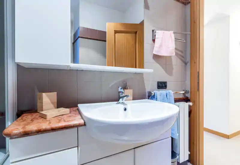 Clean, modern bathroom sink area with a large mirror, marble countertop and neatly hung towels—bright and well maintained.