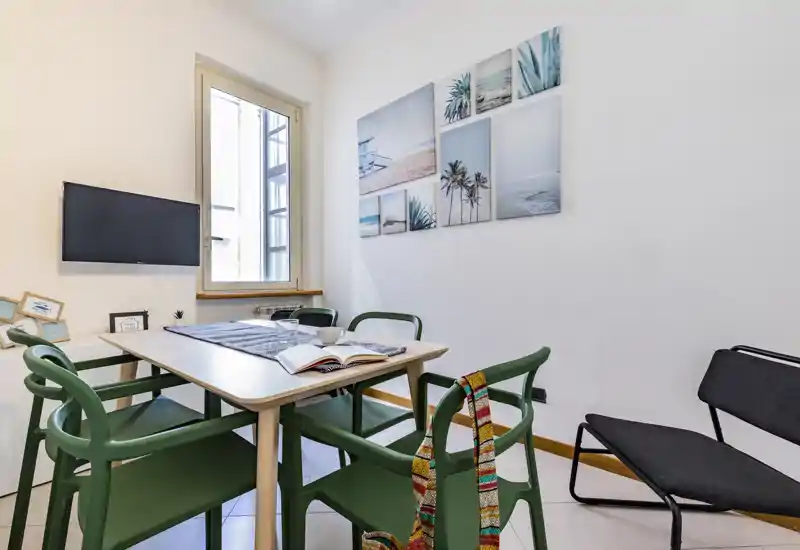 Bright, styled dining nook with a light wood table, green chairs and coastal wall art — ideal for casual meals or working by the window.