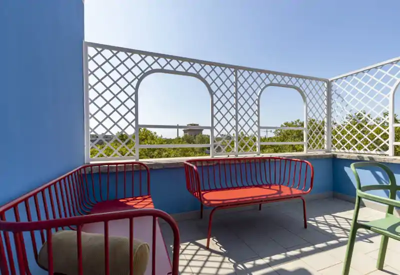 Terrasse ensoleillée avec assises métalliques colorées, garde-corps à treillis décoratif et agréable vue sur les cimes des arbres — parfaite pour se détendre dehors.