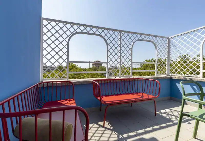 Terrasse privée ensoleillée avec bancs métalliques colorés et vue sur la cime des arbres — espace extérieur lumineux et aéré, idéal pour se détendre.