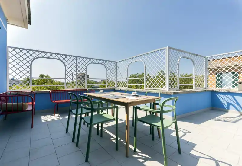 Terrasse privée ensoleillée avec table et chaises, garde-corps à treillis et ciel bleu — parfaite pour des repas en plein air et la détente.