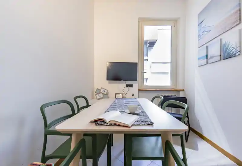 Coin repas moderne et lumineux avec table en bois, chaises vertes et tableaux muraux ; la lumière naturelle de la fenêtre rend l'espace accueillant.