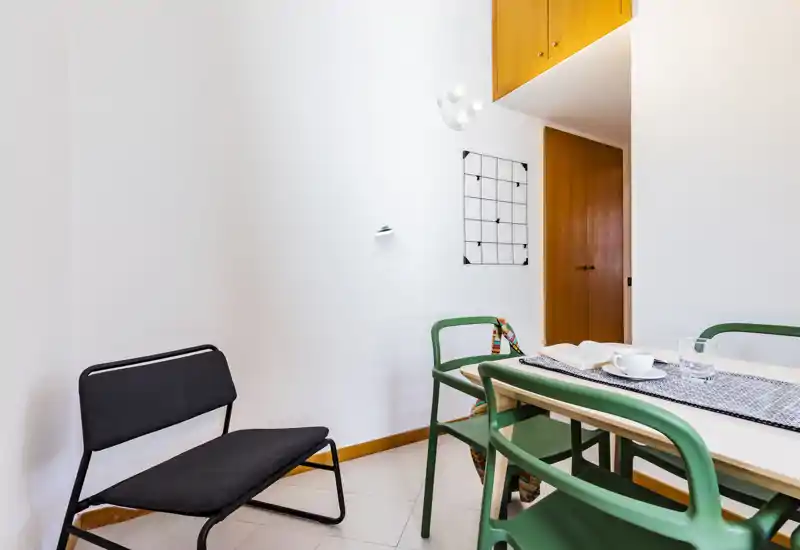 Angolo pranzo moderno e luminoso con tavolo piccolo, sedie verdi e arredo minimalista — perfetto per pasti accoglienti.