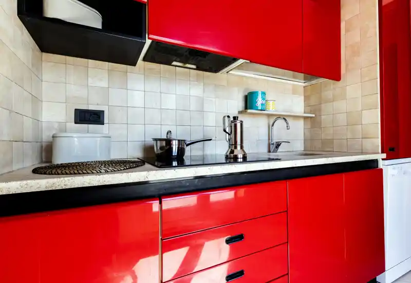 Cuisine moderne et lumineuse avec façades rouges brillantes, plaque de cuisson intégrée, évier et crédence carrelée — compacte et élégante pour la vie urbaine.