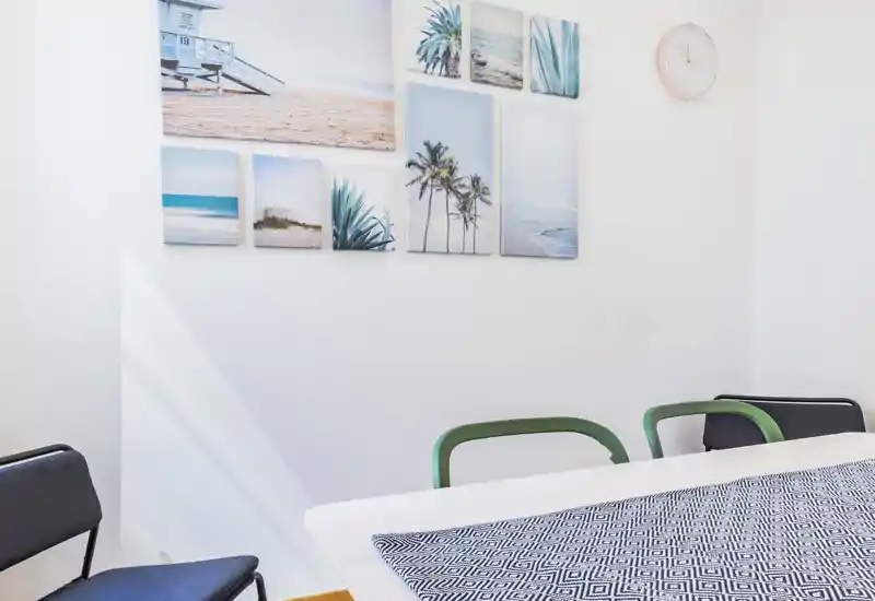 Espace repas lumineux et minimaliste avec table blanche, chemin de table à motifs et chaises variées sous des tableaux bord de mer — cadre calme et accueillant pour les repas.
