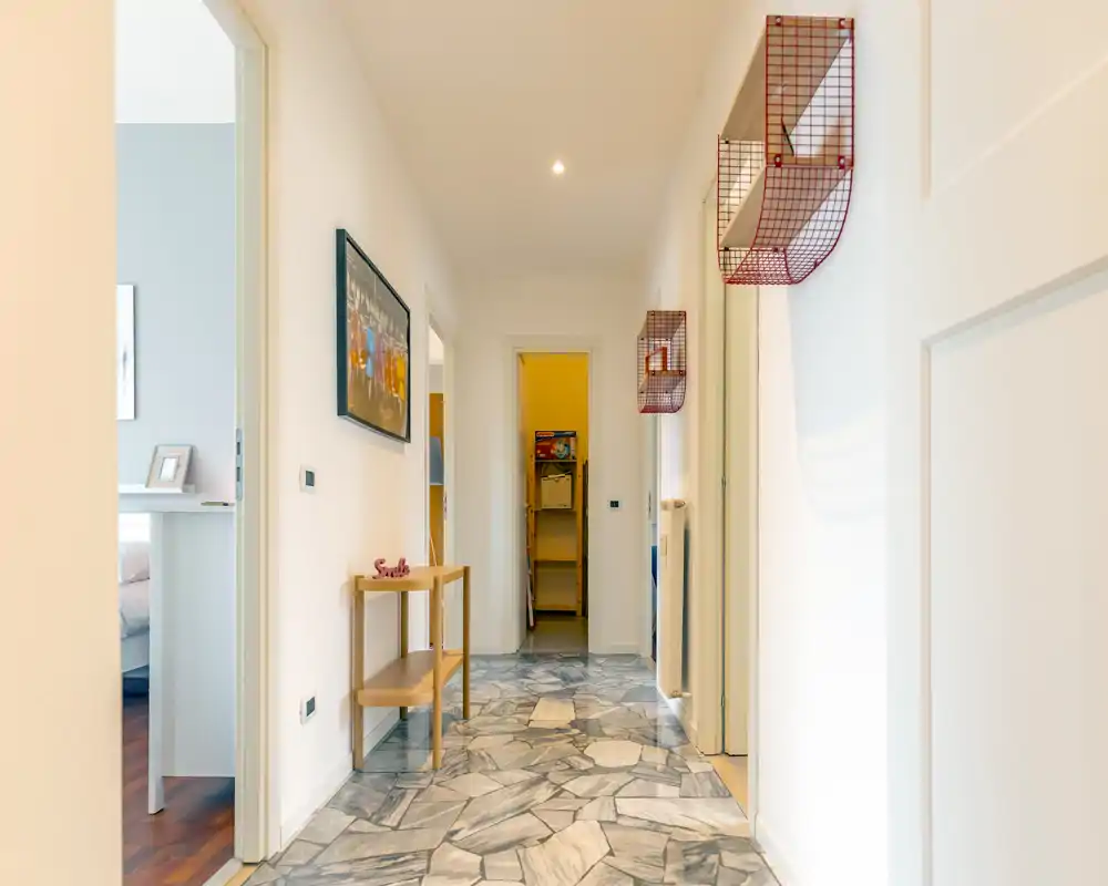 Bright, well-lit hallway/entrance with patterned stone floor, wall-mounted storage baskets and a small console table — clean and welcoming transition space.