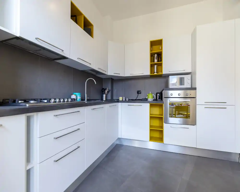 Modern, bright kitchen with white cabinetry, integrated oven and gas hob, and cheerful yellow shelving accents. Clean countertops and well-organized appliances make it ready for cooking.