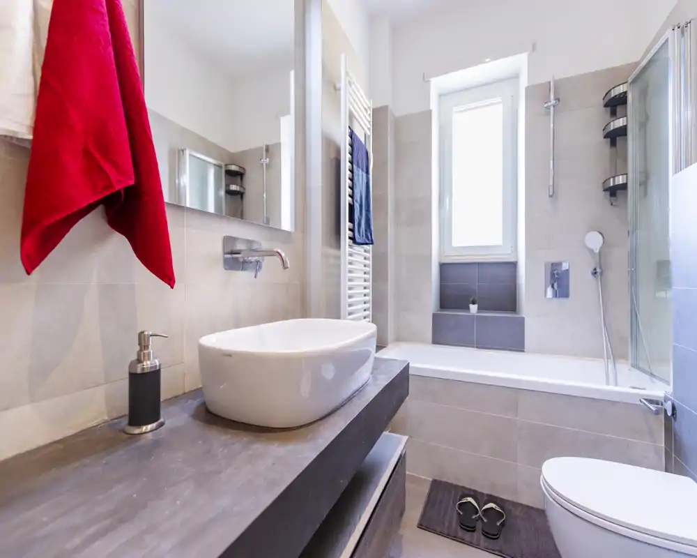 Modern, well-lit bathroom with a countertop basin, bathtub with shower, wall-mounted taps and a towel radiator; clean neutral tiles and contemporary fixtures.