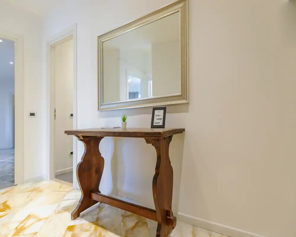 Bright, minimal entrance with a decorative wooden console table and large wall mirror—clean lines and marble-look flooring create an inviting first impression.