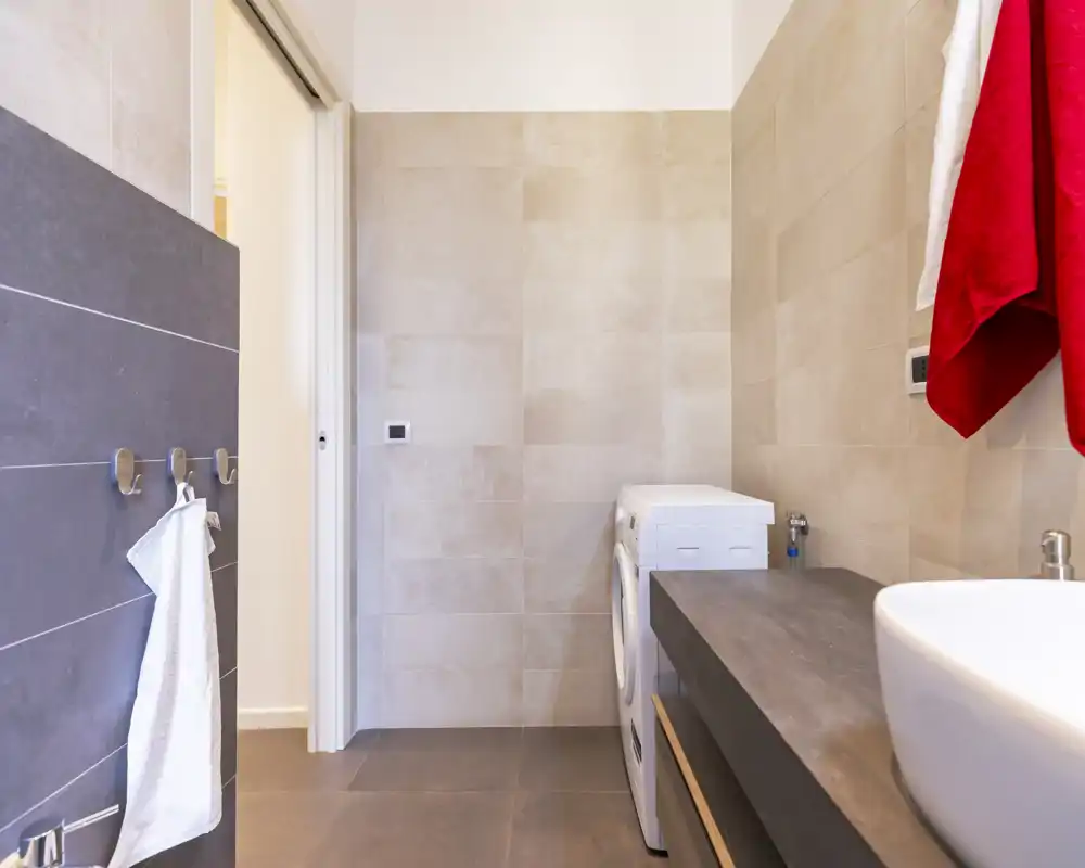 Clean modern bathroom with tiled walls, a countertop sink and a washing machine tucked beside the vanity — bright, minimal design ideal for practical stays.