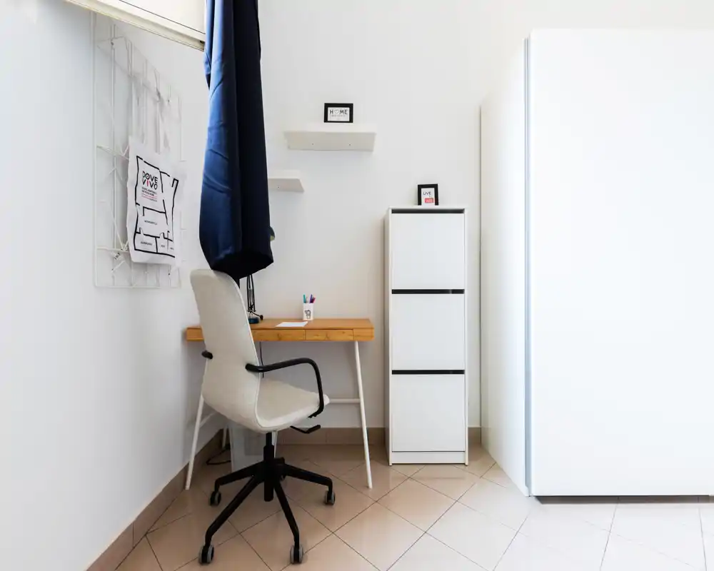 Bright, minimal living/working corner with a simple wooden desk, ergonomic chair and white storage cabinet — ideal for a tidy workspace in a small apartment.